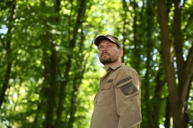 Photo of Forester in cap examining plants in forest, low angle view. Space for text