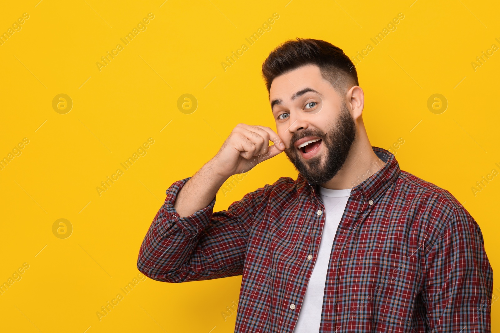 Photo of Happy young man touching mustache on yellow background. Space for text