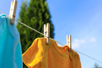 Photo of Clean baby onesies hanging on washing line in garden, closeup. Drying clothes