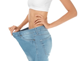 Photo of Young slim woman in old big jeans showing her diet results on white background