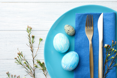 Festive Easter table setting with eggs and floral decoration on wooden background, flat lay