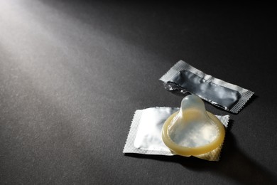 Photo of Unpacked condom and torn package on black background, space for text. Safe sex