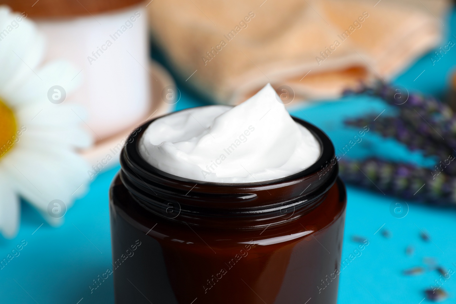 Photo of Jar of face cream and beautiful flowers on light blue table, closeup