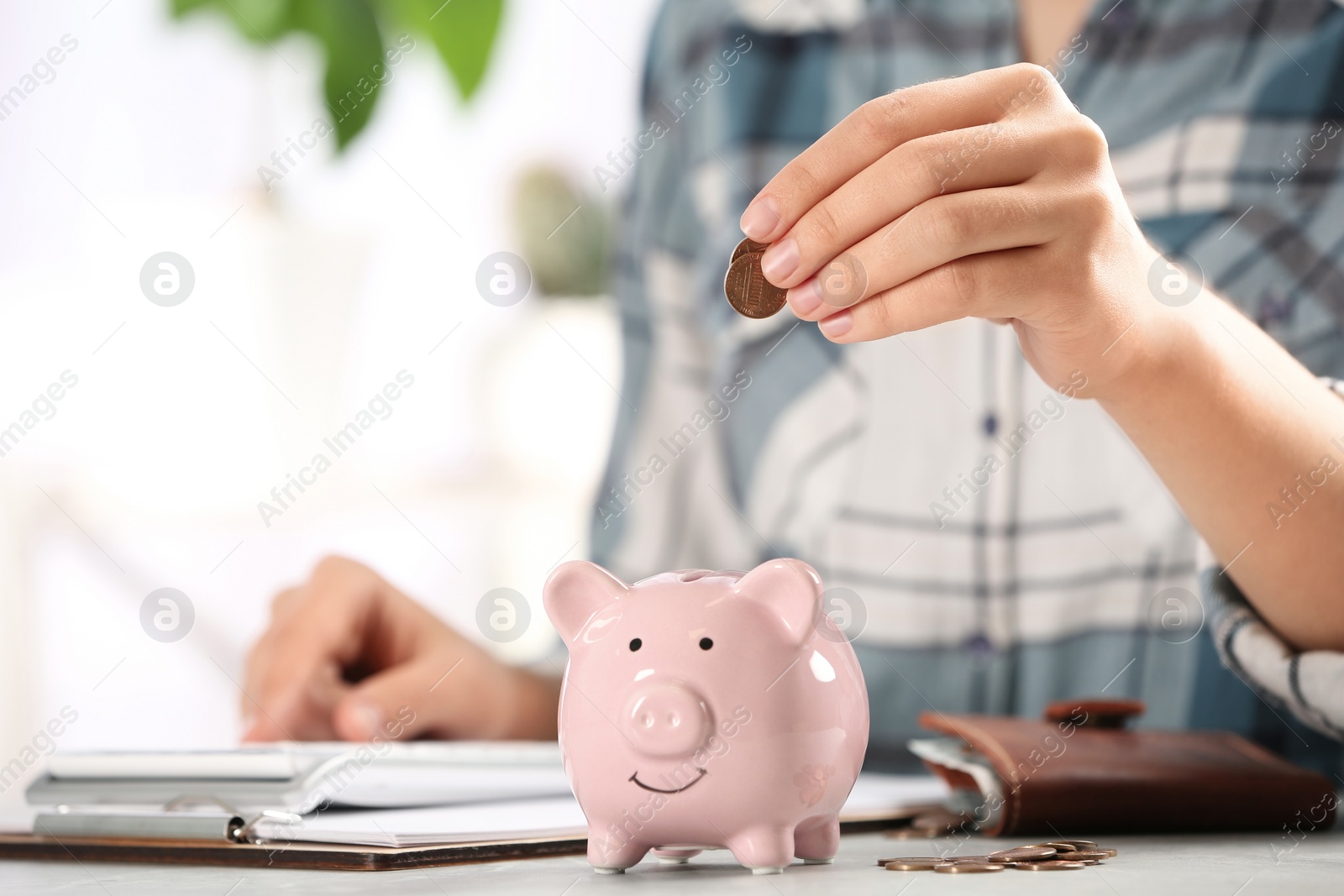 Photo of Woman putting money into piggy bank at table, closeup