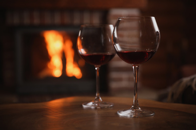 Photo of Glasses of red wine near fireplace indoors. Space for text