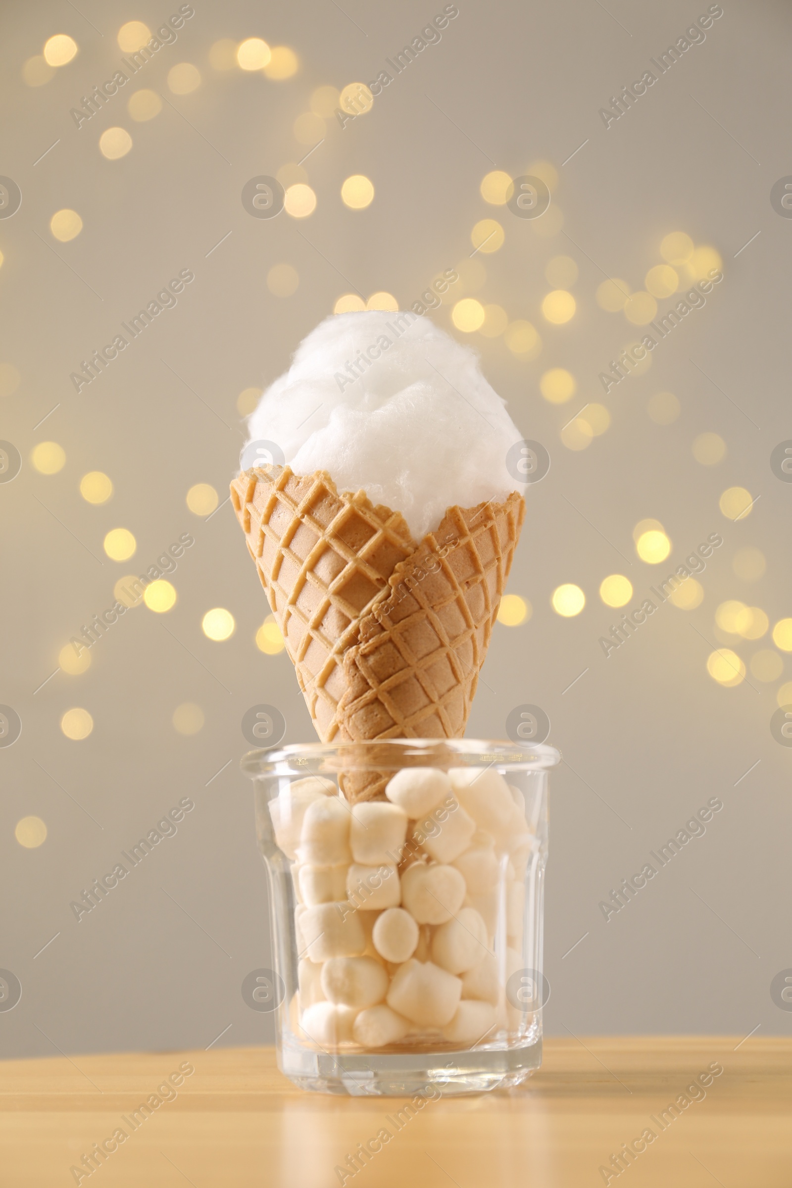 Photo of Sweet cotton candy in waffle cone on table against blurred lights