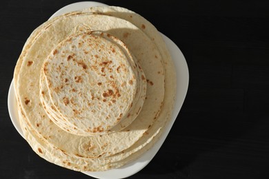 Many tasty homemade tortillas on black wooden table, top view