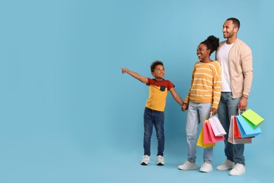 Photo of Family shopping. Happy parents and son with colorful bags on light blue background, space for text