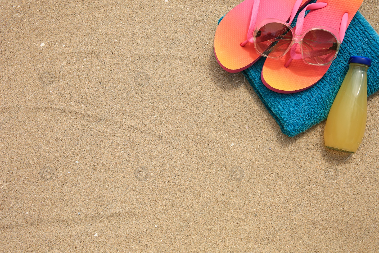 Photo of Stylish sunglasses, flip flops. towel and bottle of refreshing drink on sand, above view. Space for text