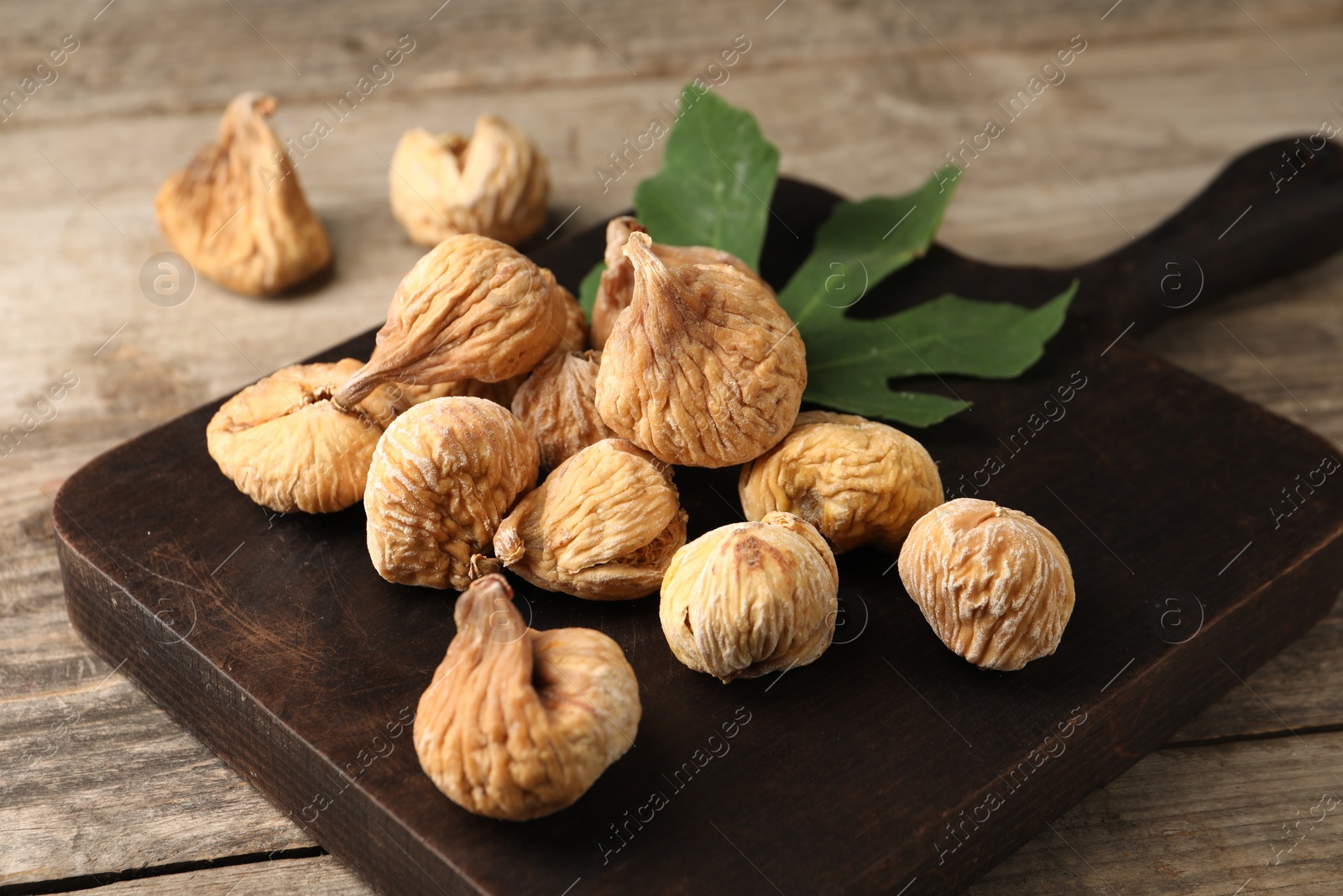 Photo of Board with tasty dried figs and green leaf on wooden table