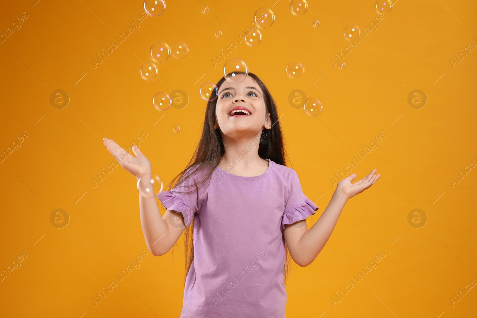 Photo of Little girl having fun with soap bubbles on yellow background