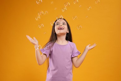 Little girl having fun with soap bubbles on yellow background