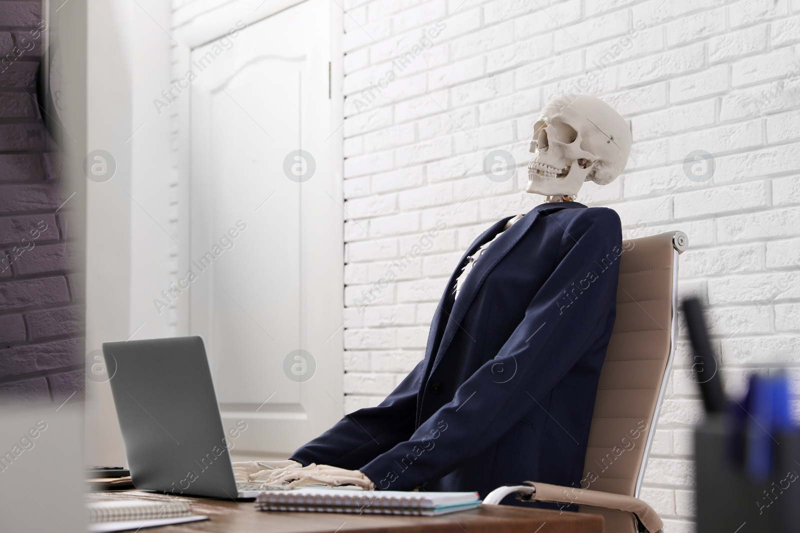 Photo of Human skeleton in suit using laptop at table in office