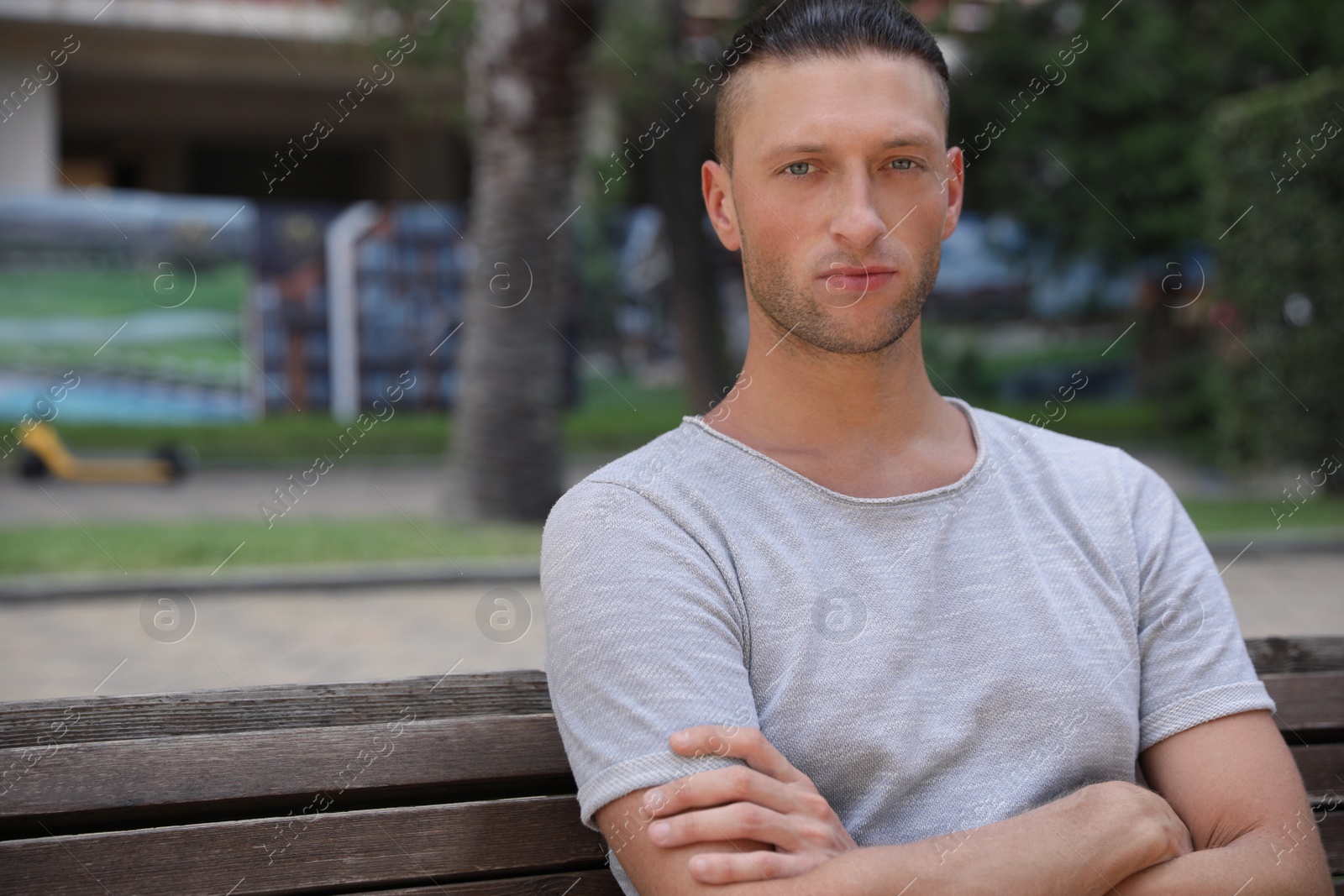 Photo of Handsome young man sitting on bench in park, space for text