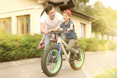 Image of Dad teaching son to ride bicycle outdoors on sunny day