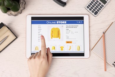 Woman with tablet shopping online at white wooden table, top view