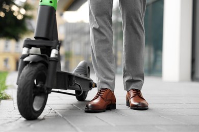 Photo of Businessman with modern kick scooter on city street, closeup