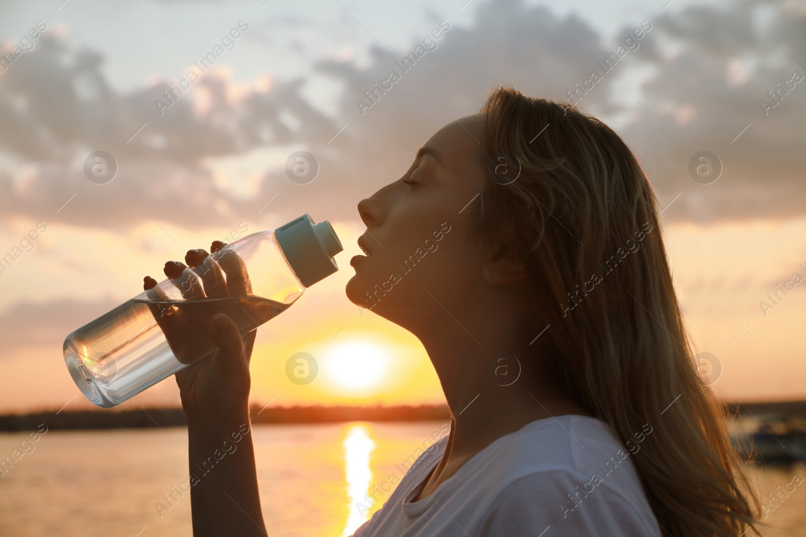 Photo of Young woman drinking water to prevent heat stroke near river at sunset