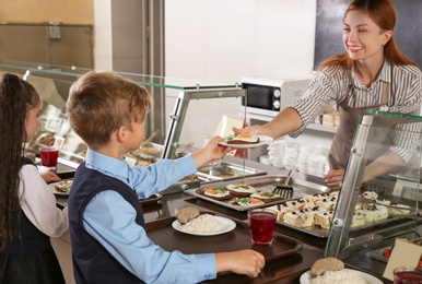 Photo of Woman giving plate with healthy food to boy in school canteen