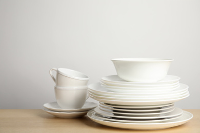 Photo of Clean plates, bowl and cups on wooden table against white background. Space for text