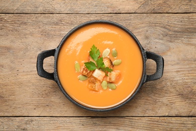 Photo of Tasty creamy pumpkin soup with croutons, seeds and parsley in bowl on wooden table, top view