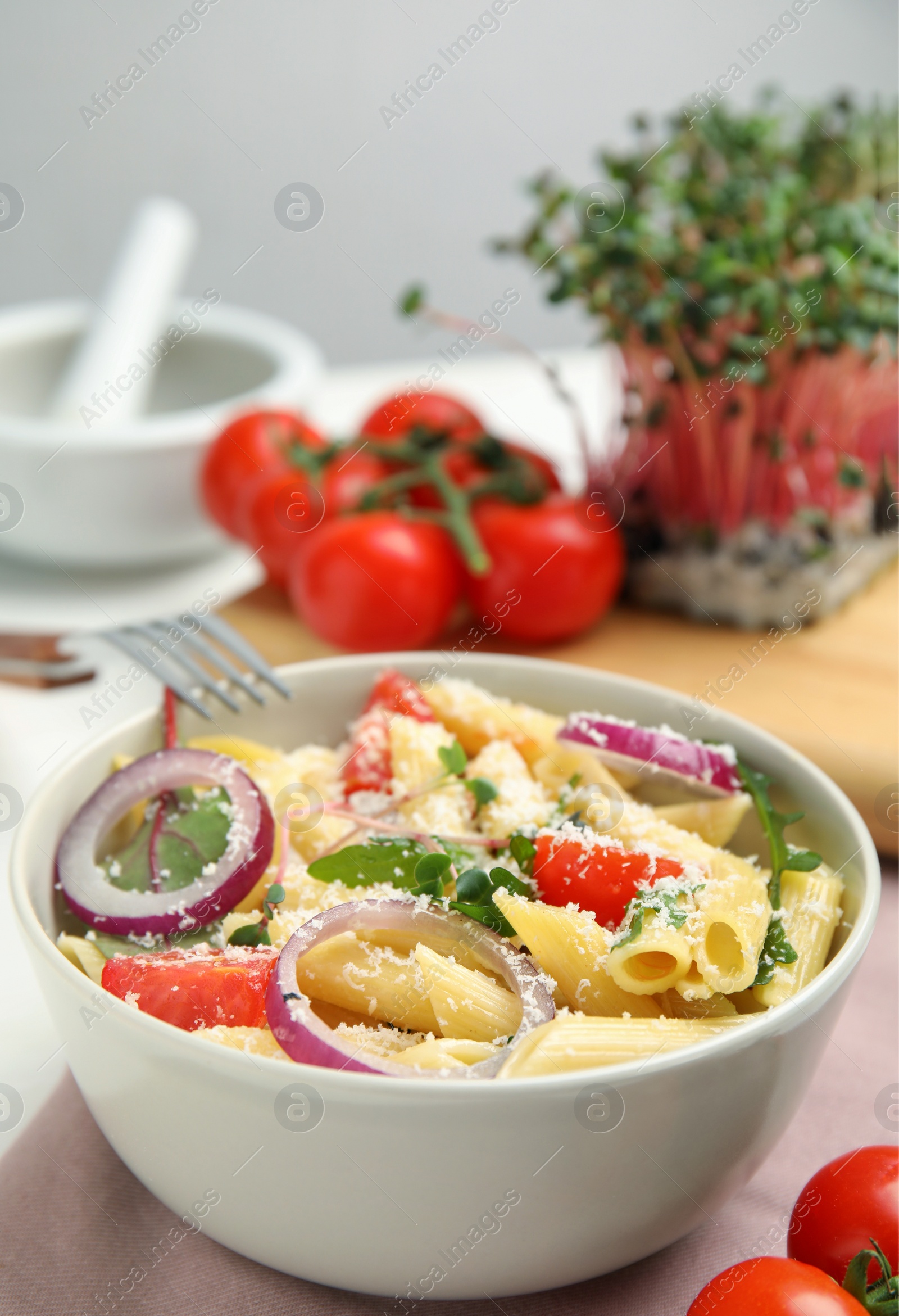 Photo of Bowl of delicious pasta with tomatoes, onion and cheese on table, closeup
