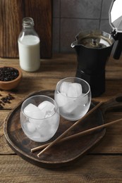 Photo of Making iced coffee. Ice cubes in glasses and straws on wooden table