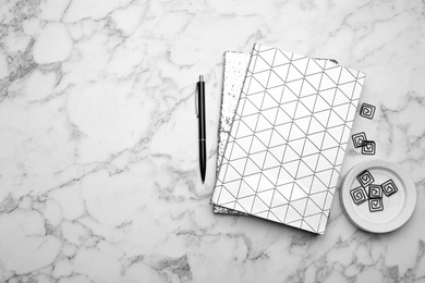 Stylish notebooks and pen on white marble table, flat lay. Space for text
