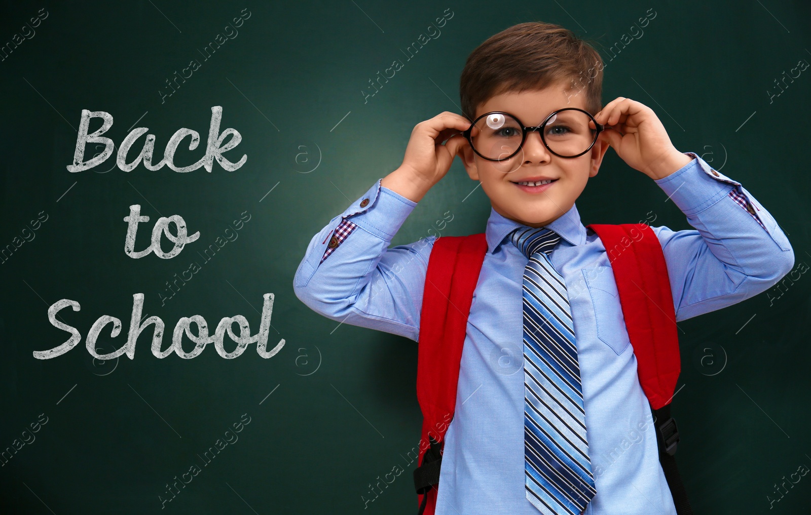 Image of Cute little child wearing glasses near chalkboard with phrase BACK TO SCHOOL