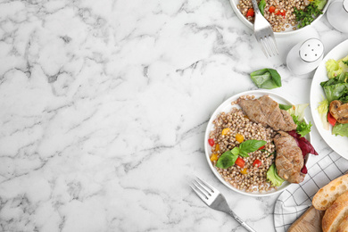 Tasty buckwheat porridge with meat on white marble table, flat lay. Space for text