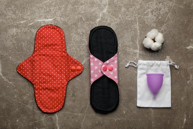 Photo of Reusable cloth pads, menstrual cup and cotton flower on brown table, flat lay
