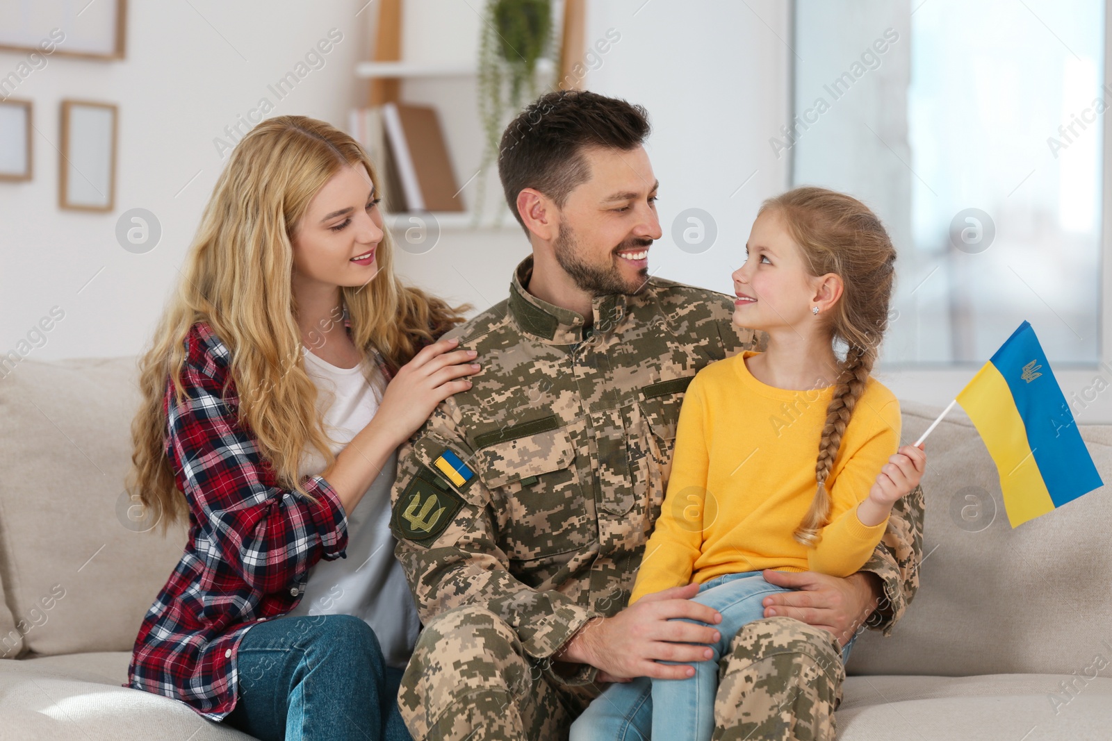 Photo of Soldier in military uniform reunited with his family and Ukrainian flag on sofa at home