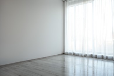 Empty room with white wall, large window and wooden floor