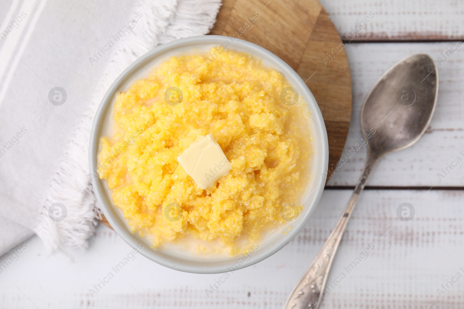 Photo of Tasty cornmeal with butter in bowl served on white wooden table, flat lay