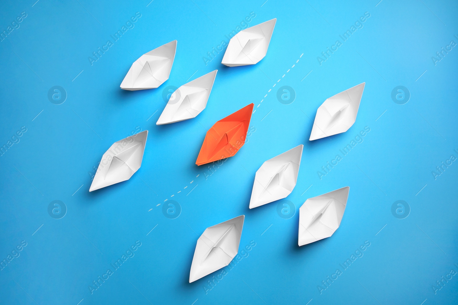 Photo of Orange paper boat floating between others on light blue background, flat lay. Uniqueness concept