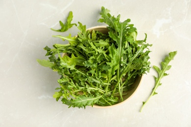 Fresh arugula in bowl on light grey marble table, flat lay