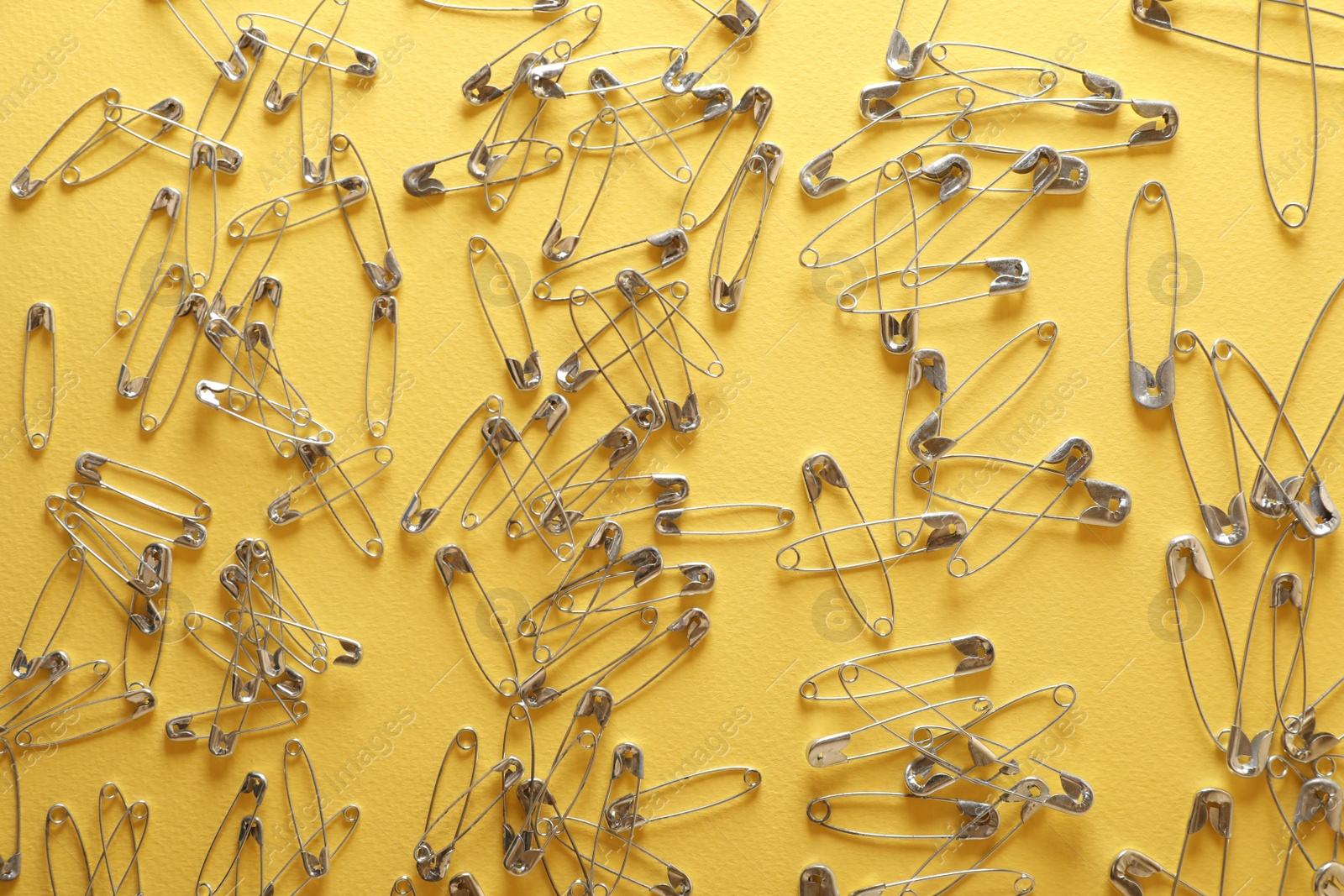 Photo of Many safety pins on yellow background, flat lay