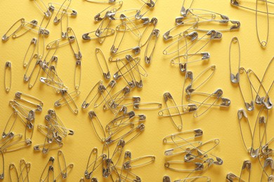 Many safety pins on yellow background, flat lay