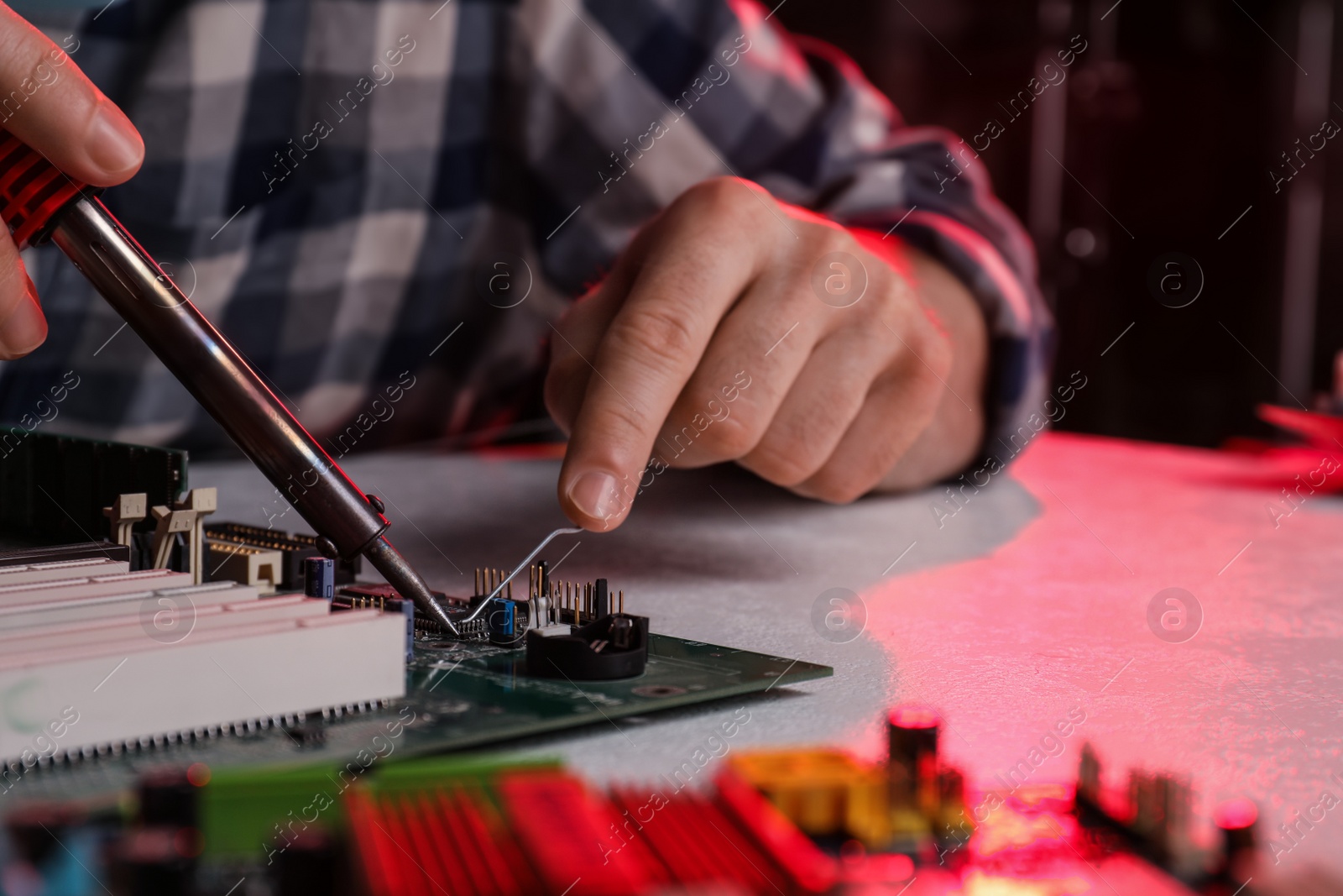 Photo of Technician repairing electronic circuit board with soldering iron at table, closeup