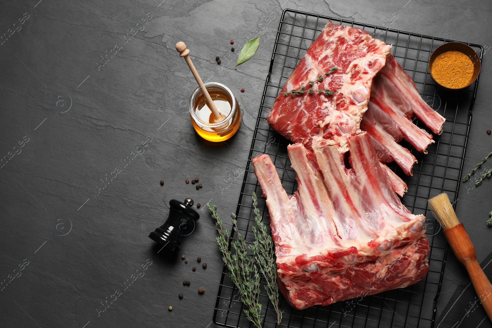 Photo of Raw ribs with thyme and pepper on black table, flat lay