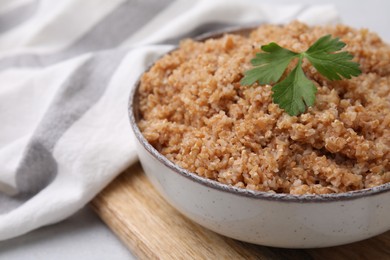 Tasty wheat porridge with parsley in bowl on table, closeup. Space for text