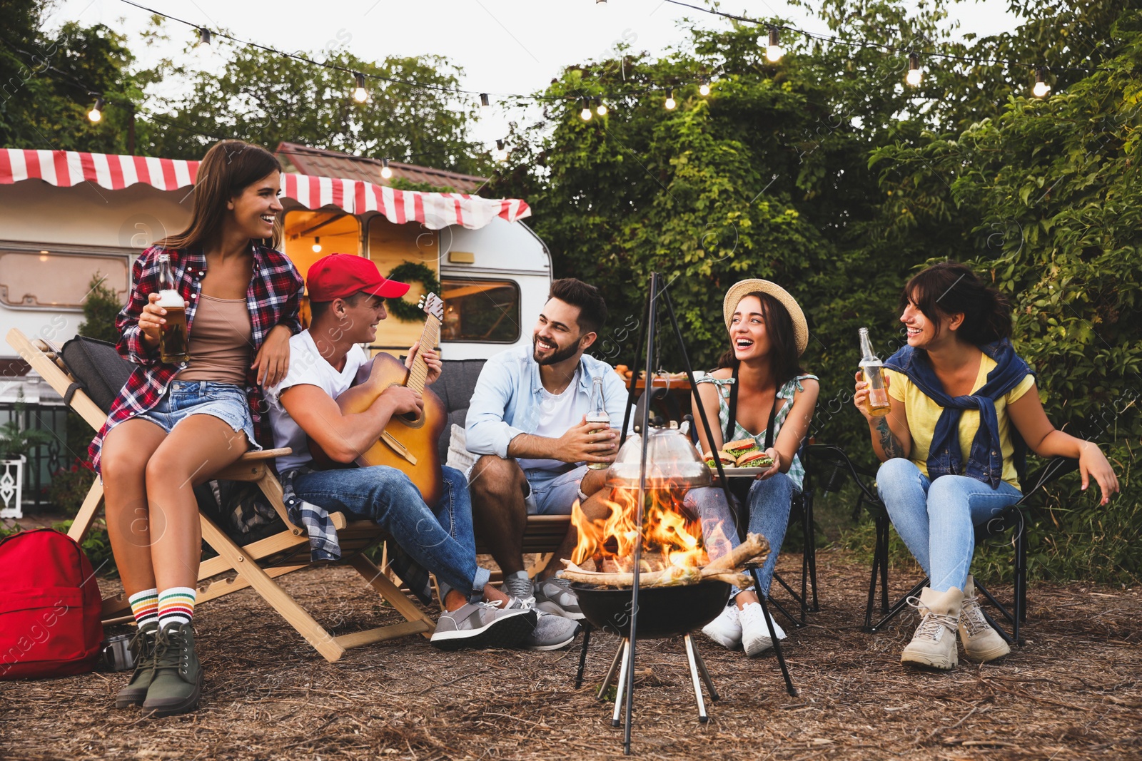 Image of Happy friends sitting near bonfire. Camping season