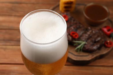 Glass of beer, delicious fried steak and sauce on wooden table, closeup. Space for text