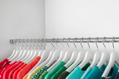 Photo of Hangers with different colorful clothes on rack in wardrobe