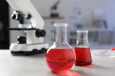 Photo of Laboratory analysis. Flasks with red liquid, petri dish and microscope on light grey table