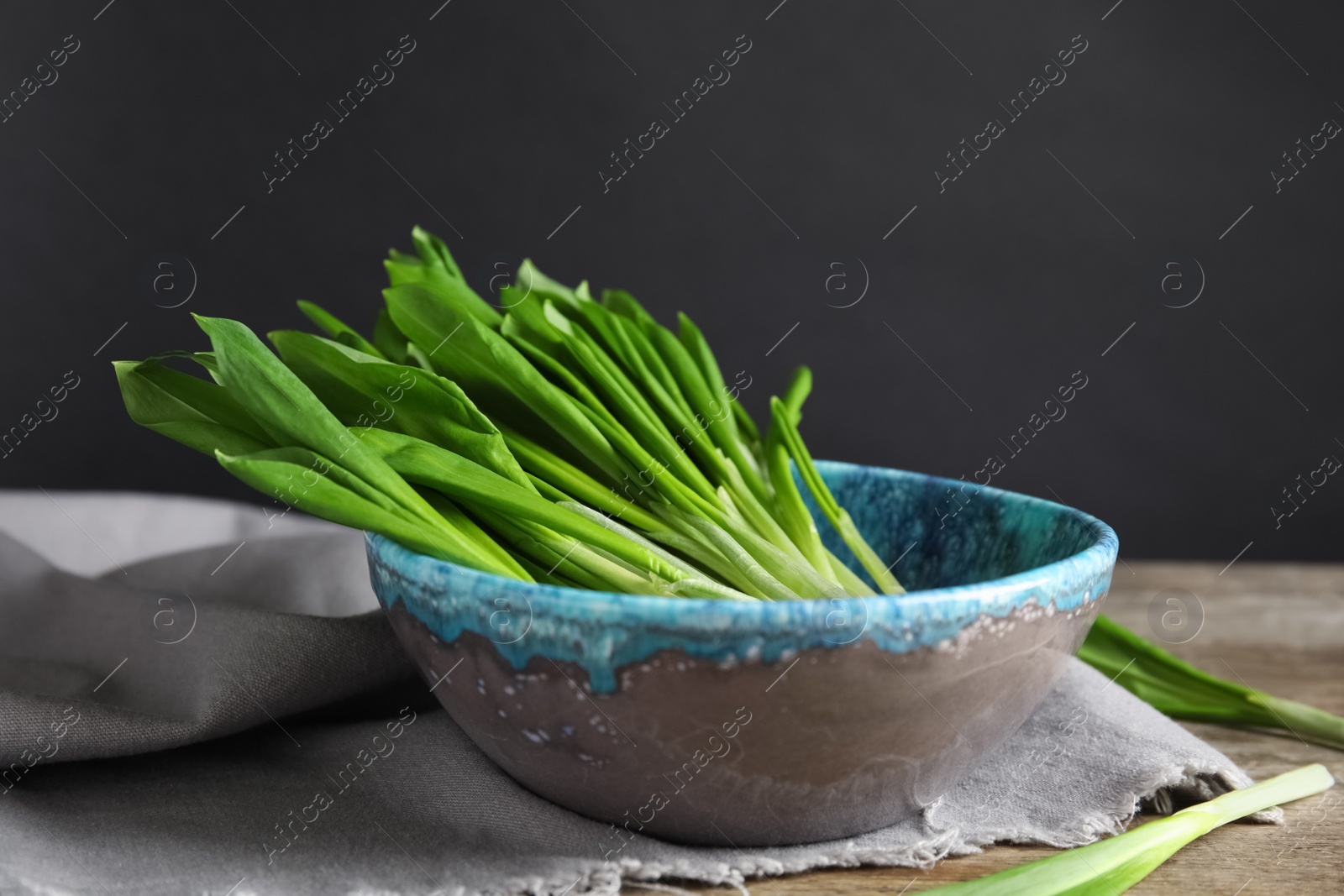 Photo of Bowl with wild garlic or ramson on wooden table against black background. Space for text