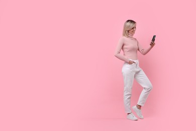 Happy woman with phone on pink background, space for text