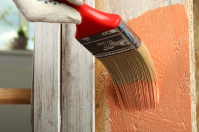 Photo of Worker applying coral paint onto wooden surface, closeup