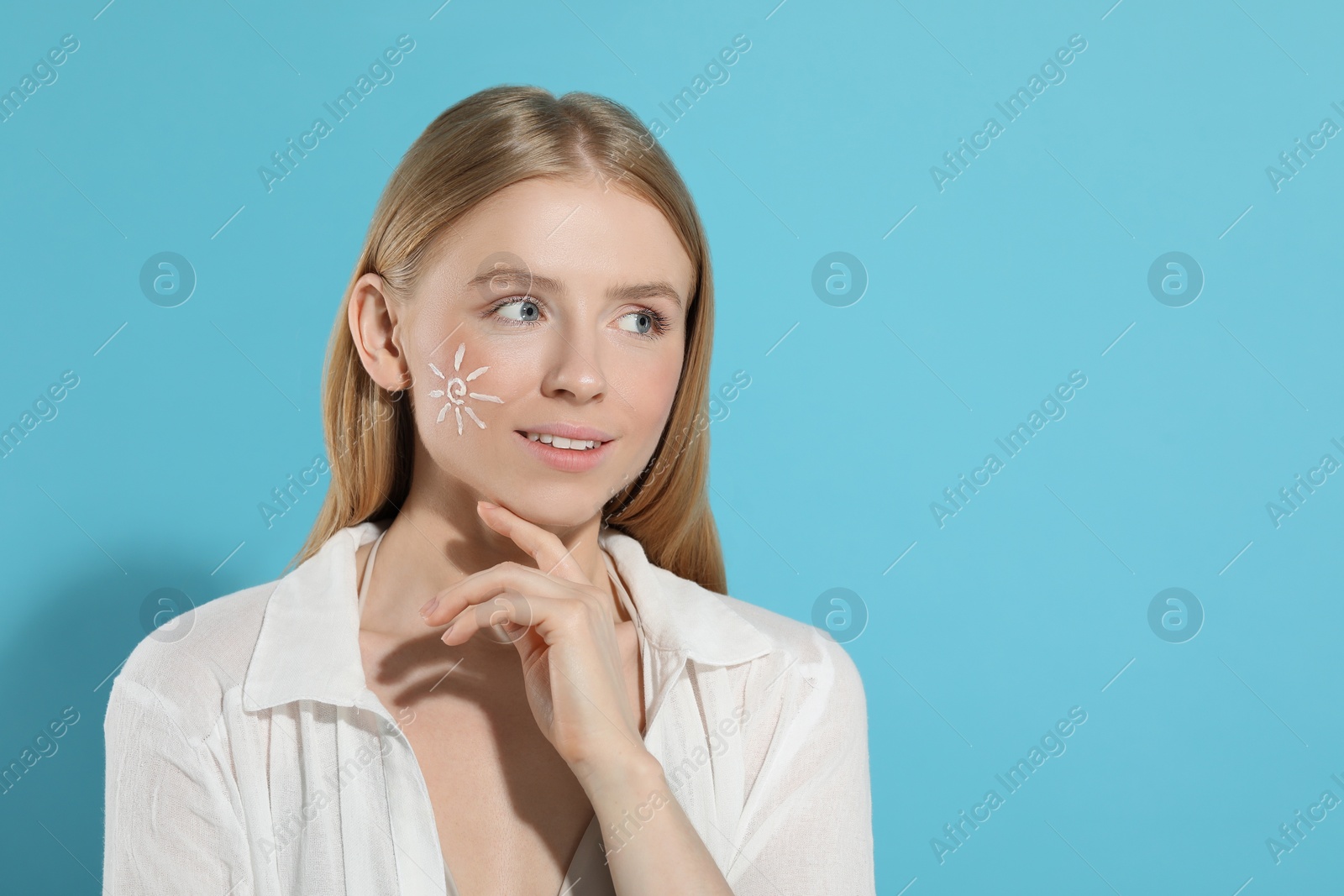 Photo of Beautiful young woman with sun protection cream on her face against light blue background, space for text