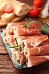 Photo of Rolled slices of delicious jamon with rosemary on wooden table